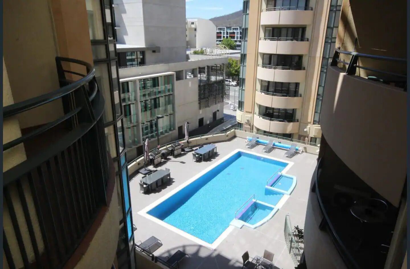 Una piscina en la azotea con sillones de descanso y un pequeño jacuzzi, rodeada de edificios modernos.