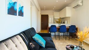 A modern living room with a black sofa, a coffee table with a magazine and a vase, and a dining area with chairs and a kitchen in the background. - Phaedrus Living: Seaside Residence Lighthouse 70 (Paphos)