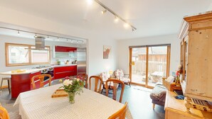 Una cocina amplia con armarios rojos, un comedor con mesa lista para cuatro personas, y un gran armario de madera.