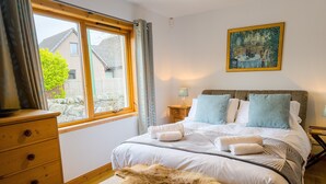 Un dormitorio con cama, cómoda de madera, manta de piel, un cuadro y una ventana con cortinas.