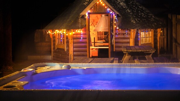 Una cabaña rústica de madera con jacuzzi y luces de cadena.