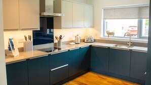 Een moderne keuken met donkerblauwe kastjes, een roestvrijstalen afzuigkap, een magnetron en een raam met uitzicht op een rode auto buiten.