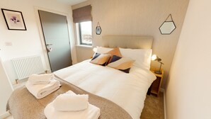 Een netjes opgemaakt bed met hoofdbord, een bedlampje en een raam met uitzicht.