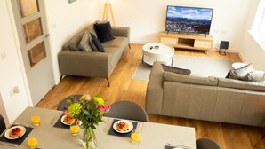 Een moderne woonkamer met een bank, een ontbijt klaar dektafel, een televisie en uitzicht op een stadsgezicht.