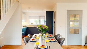 Een ontbijtruimte met een gedekte tafel, een vaas met bloemen en een keuken op de achtergrond.