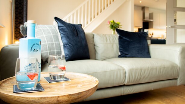 Een woonkamer met een bank, een houten bijzettafeltje en een fles gin.