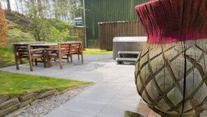 En uteplats med ett träbord och stolar, en grill och en dekorativ vas.