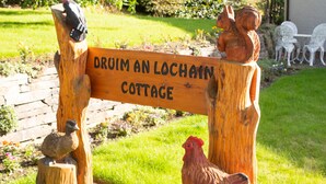 En träskylt med texten ”DROOM AN LOCHAIN COTTAGE” och en skulptur av en höna.
