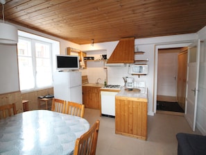 A compact kitchen with wooden cabinets, a built-in microwave, a gas stove, and a dining area with a round table and chairs.