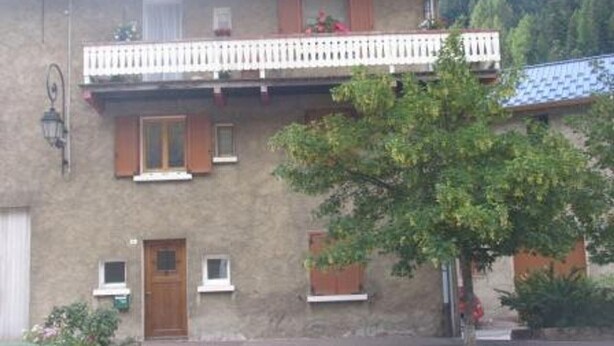 Un edificio de dos plantas con balcón, ventanas con contraventanas y fachada de piedra.