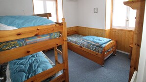Una habitación pequeña y acogedora con dos literas de madera y una cama individual, que cuenta con una ventana y una repisa con una caja.
