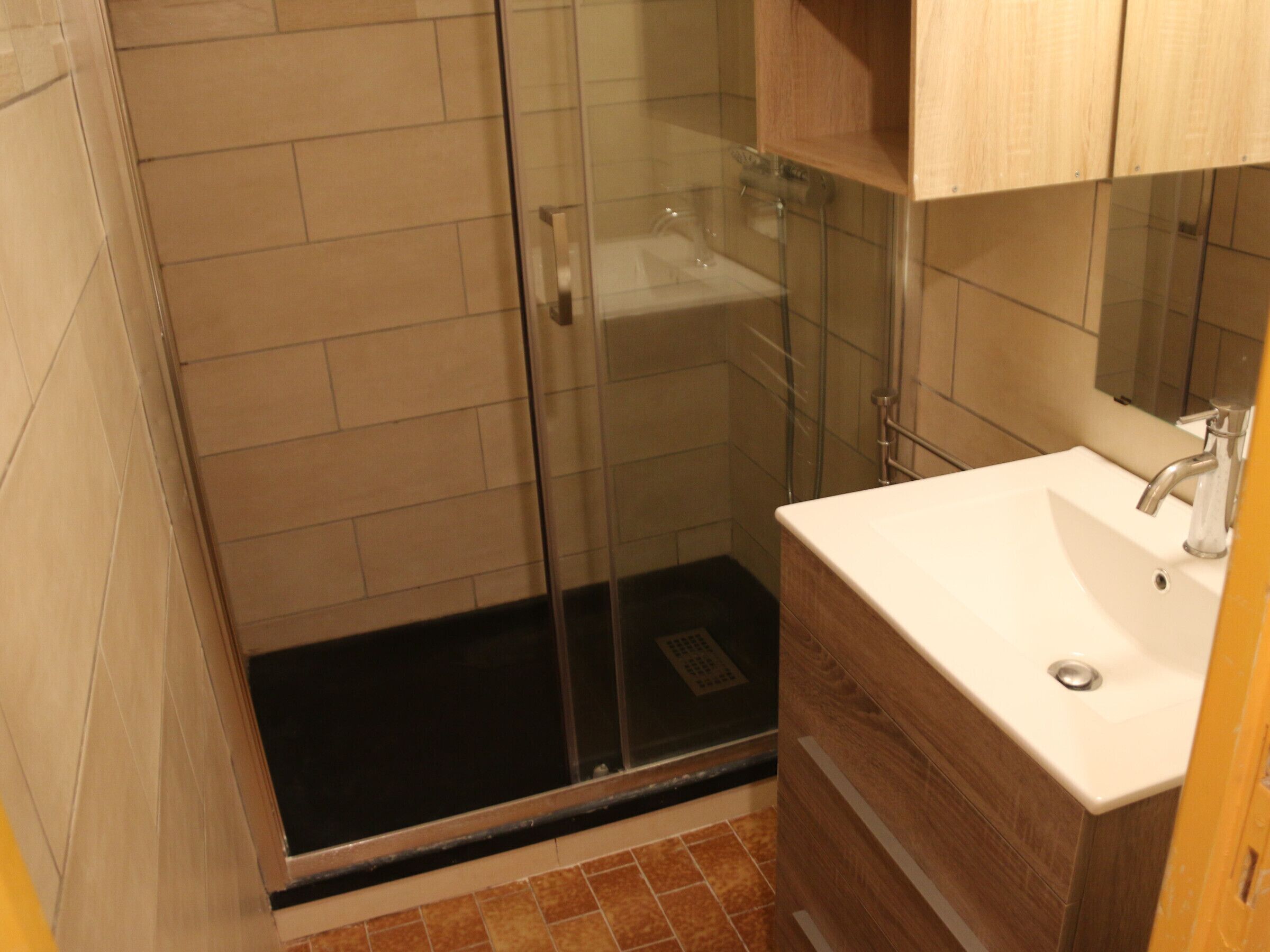 A bathroom with a glass shower enclosure, a white sink, and wooden cabinetry.