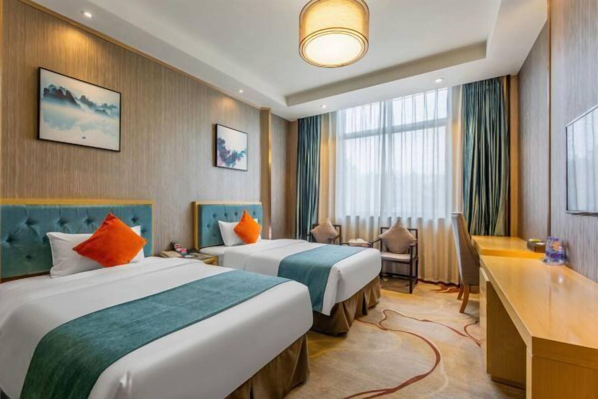 A hotel room with two beds, a desk, a chair, and a large window with curtains.