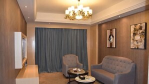Ein Zimmer mit einer Chandelier, zwei Sesseln, einem Sofa, einem kleinen runden Tisch und einem großen Fenster mit Vorhängen.
