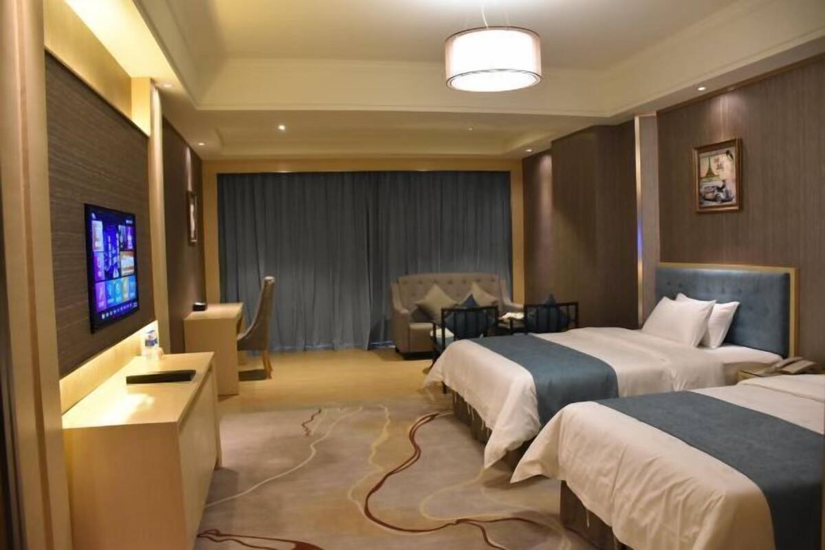 A hotel room with two beds, a desk with a computer, a TV, and a large window with curtains.
