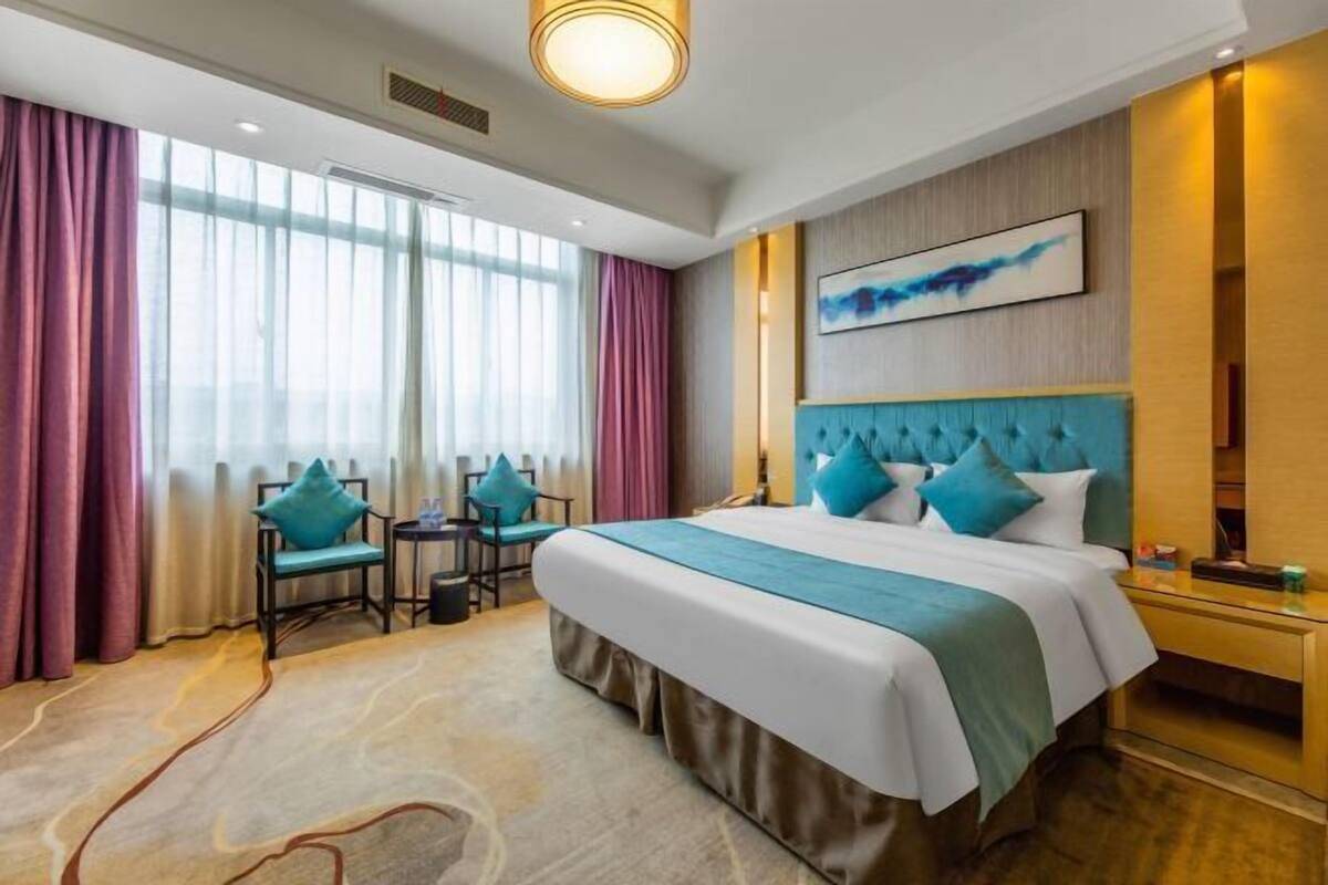 A hotel room with a large bed, a desk, a chair, and a view of the city.