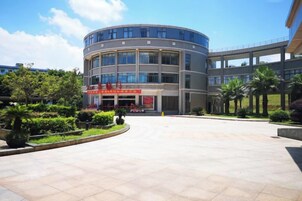 Un edificio moderno con fachada curva, entrada central y un patio ajardinado con palmeras.