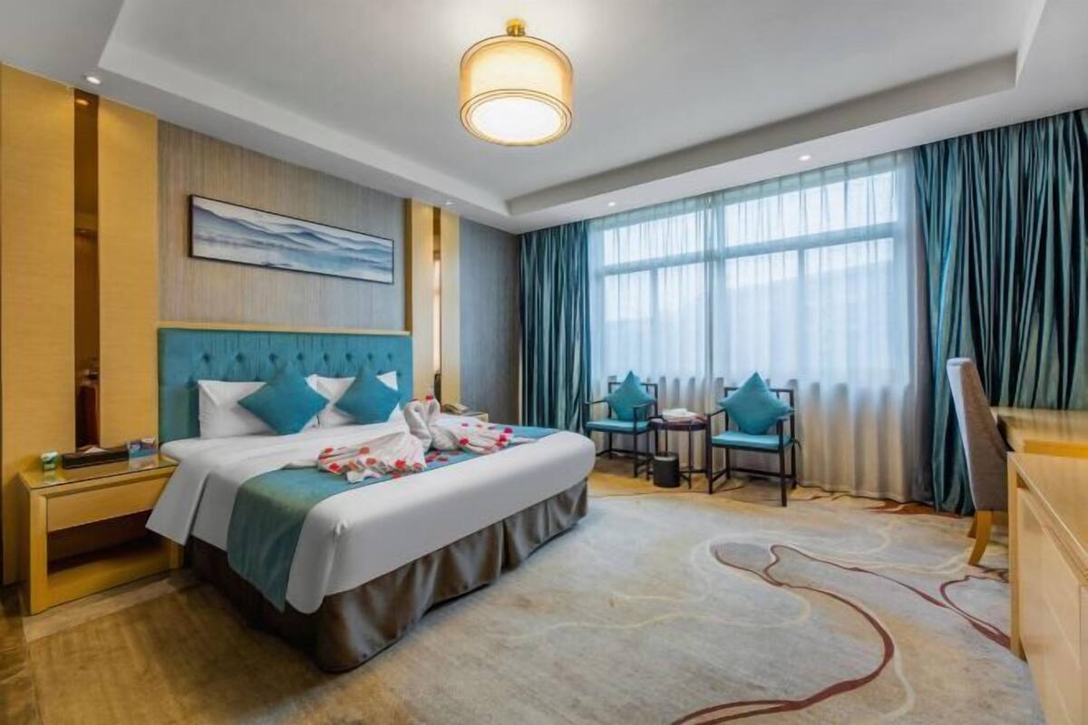 A hotel room with a bed, a desk, a chair, a small table, and a window with curtains.