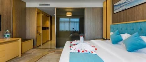 Une chambre d’hôtel avec un grand lit, une commode en bois, une salle de bain visible à travers une porte ouverte et un tableau accroché au mur.