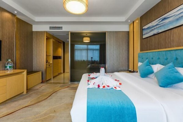 A hotel room with a large bed, a wooden dresser, a bathroom visible through an open door, and a painting on the wall. - Gannan Normal University International Academic Exchange Center (Ganzhou)