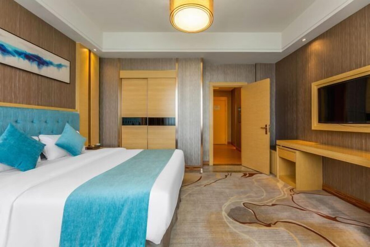 A modern hotel room with a large bed, a flat-screen TV, a wardrobe, and a door leading to another room.