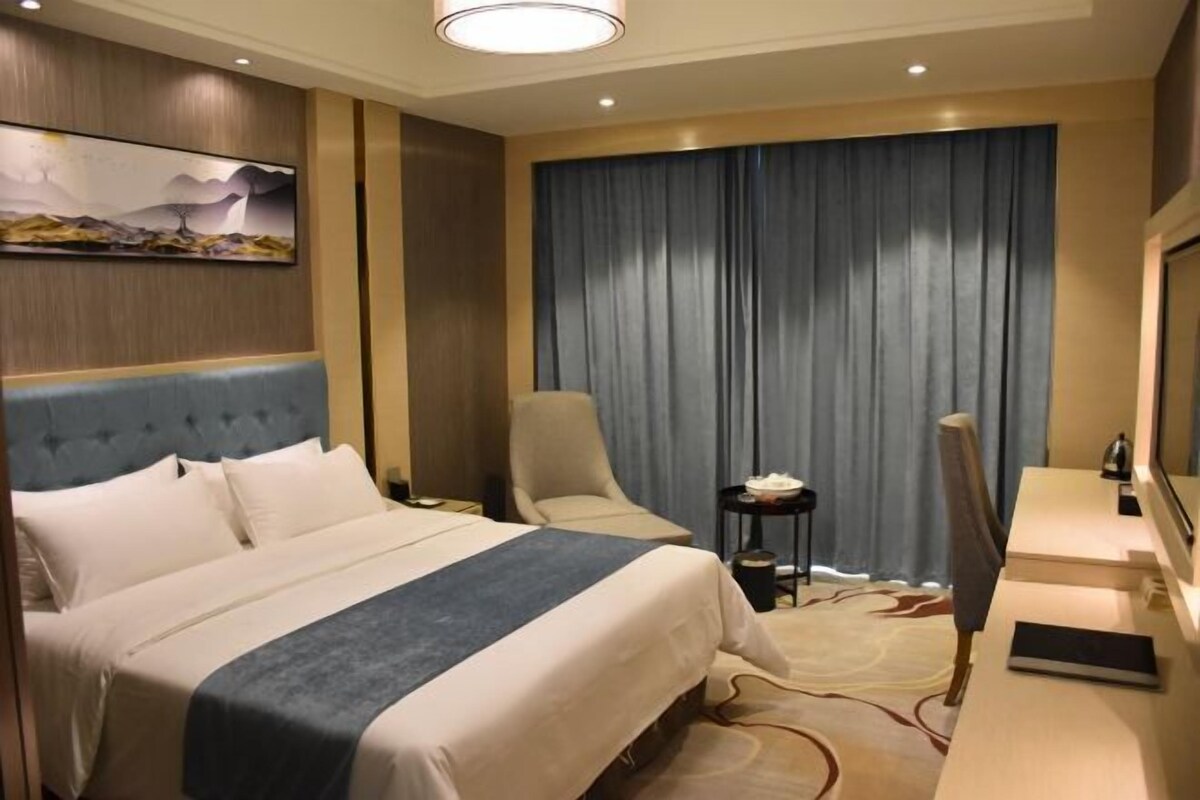 A hotel room with a large bed, a desk with a chair, a television, and a painting on the wall.