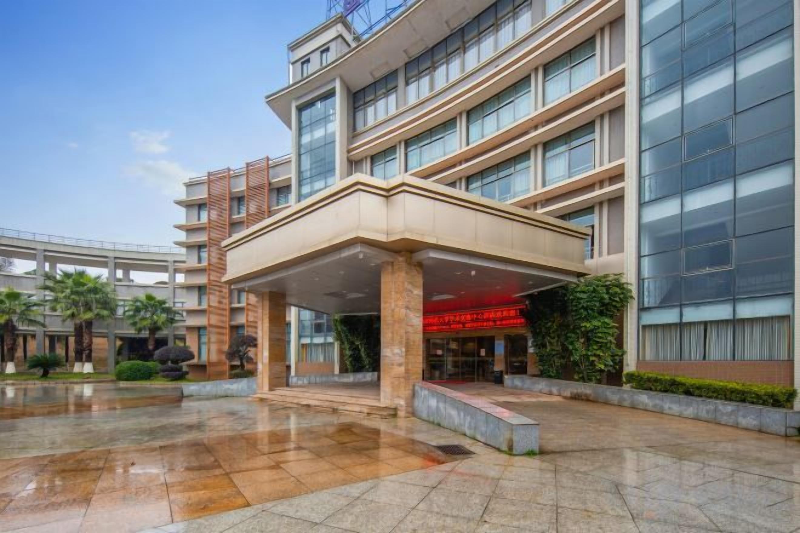 A multi-story hotel with a covered entrance, a glass facade, and a wet ground surface.