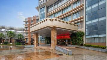 A multi-story hotel with a covered entrance, a glass facade, and a wet ground surface.