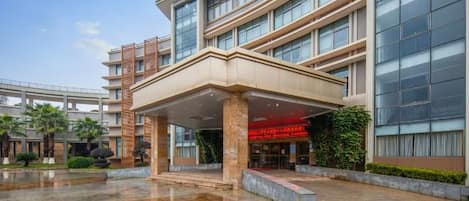A multi-story hotel with a covered entrance, a glass facade, and a wet ground surface.