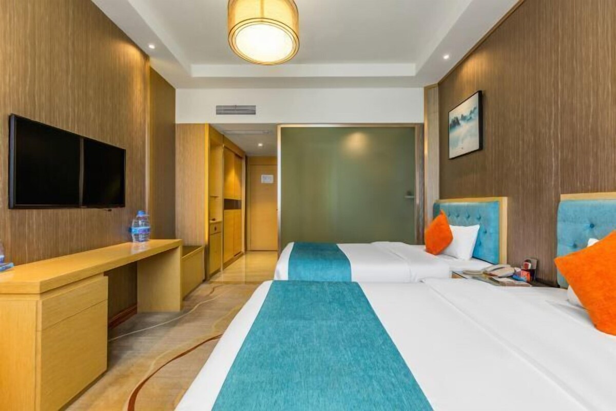 A hotel room with a bed, bedside table, TV, and a view of the hallway.