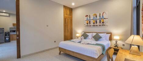 A bedroom with a wooden bed, a dining table, a kitchen area, and a painting on the wall.