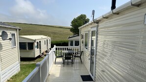 A deck with a table and chairs, surrounded by mobile homes with white siding.