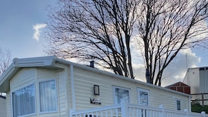 A mobile home with a white exterior, a fenced deck, and a small garden area.