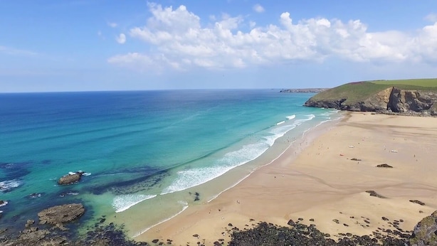 A coastal beach with clear turquoise waters, sandy shore, and rocky outcrops.