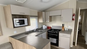 A compact kitchen with a microwave, stove, sink, and wooden cabinetry.