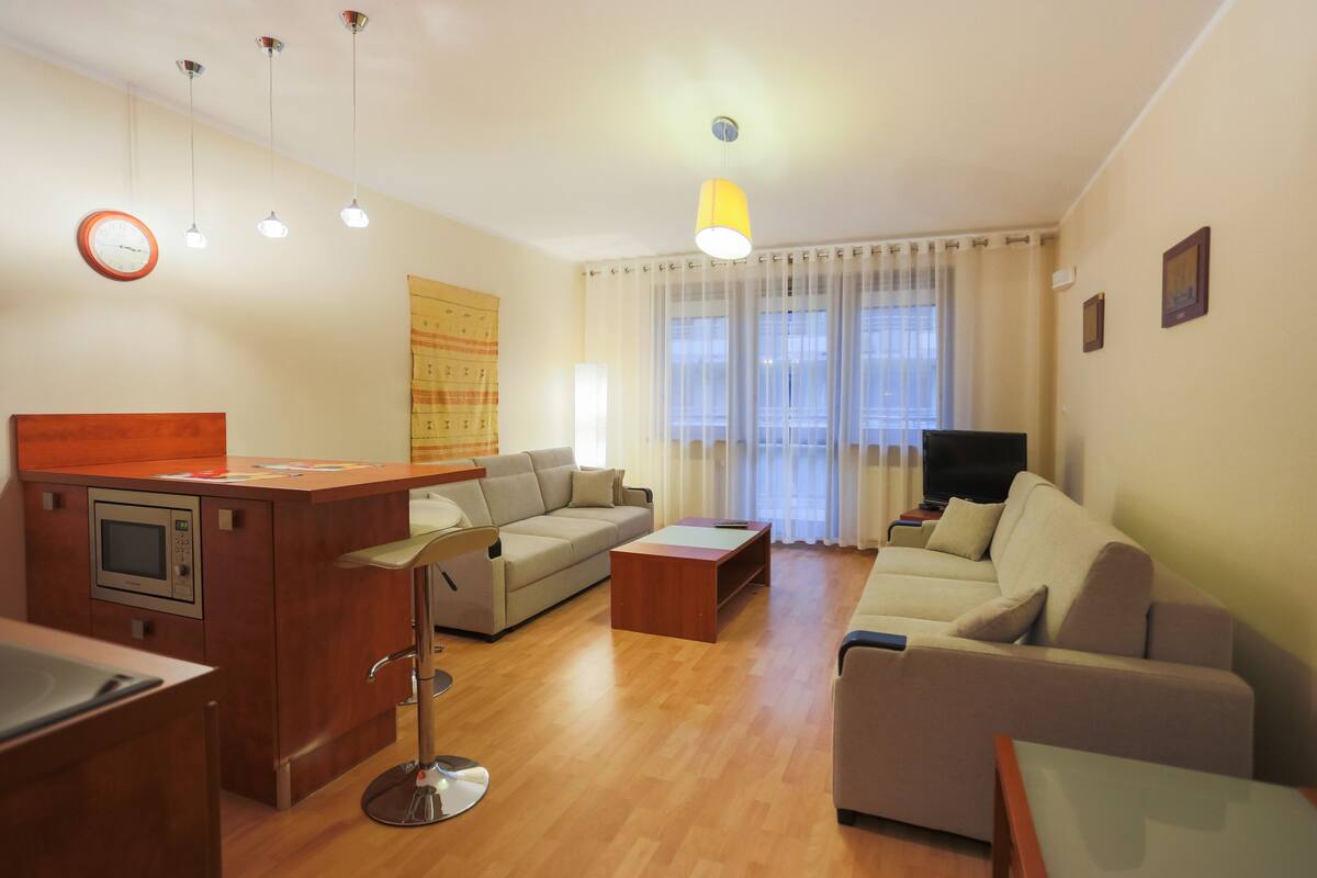 Ein modernes Wohnzimmer mit einer Couch, einem Couchtisch, einem Fernseher und einer Küchenzeile mit einer Mikrowelle.