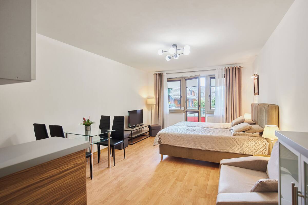 Ein modernes Hotelzimmer mit Bett, Sofa, Schreibtisch mit Stuhl, Fernseher und einem Fenster mit Vorhängen.