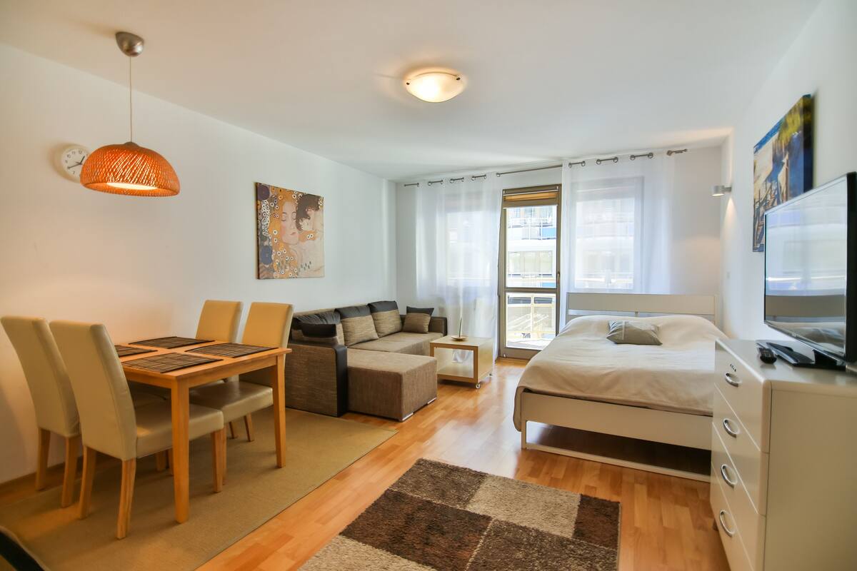 Ein moderner, hell eingerichteter Raum mit Esstisch, Sofa und Bett.