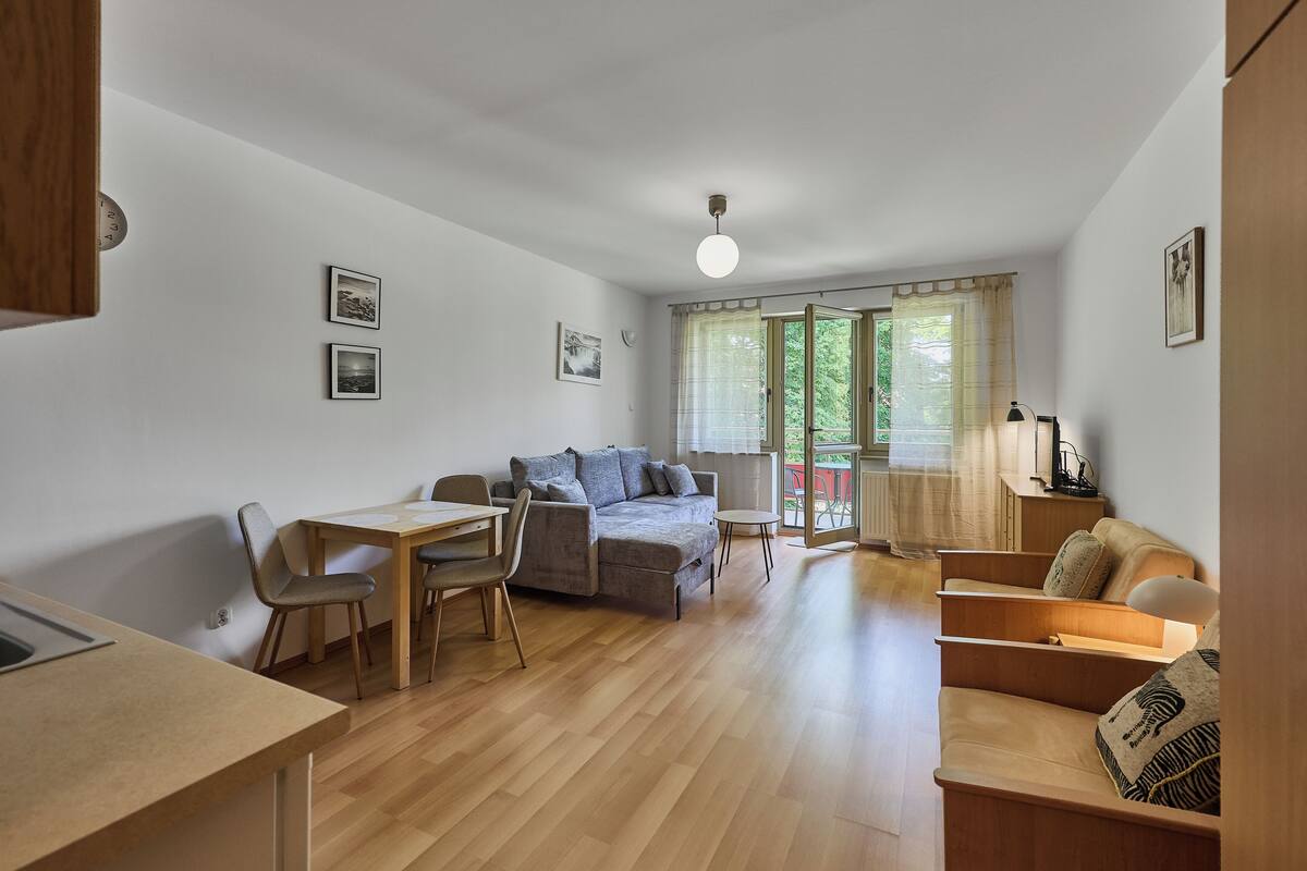 Ein modernes Wohnzimmer mit einer Couch, einem Esstisch und Stühlen. An den Wänden hängen Bilder in Rahmen, und ein Fenster ist mit Vorhängen versehen.