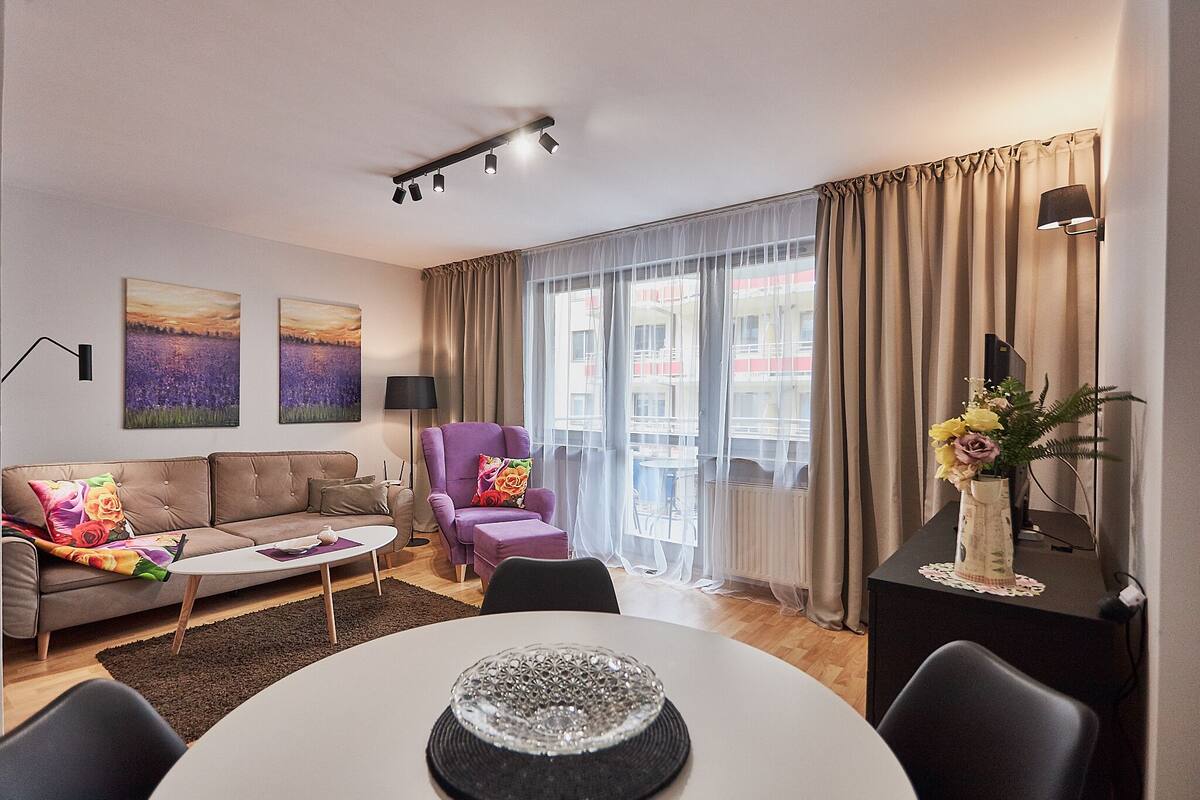 Ein modernes Wohnzimmer mit Sofa, Sessel, Couchtisch und einem Essbereich mit Tisch und Stühlen.