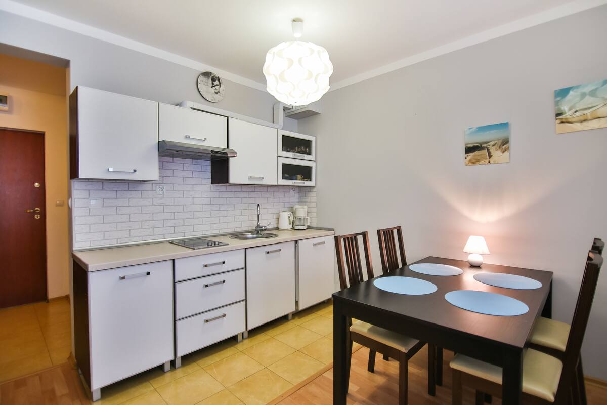 Eine moderne Küche mit weißen Schränken, einem eingebauten Backofen und einem Essbereich mit Tisch und Stühlen.