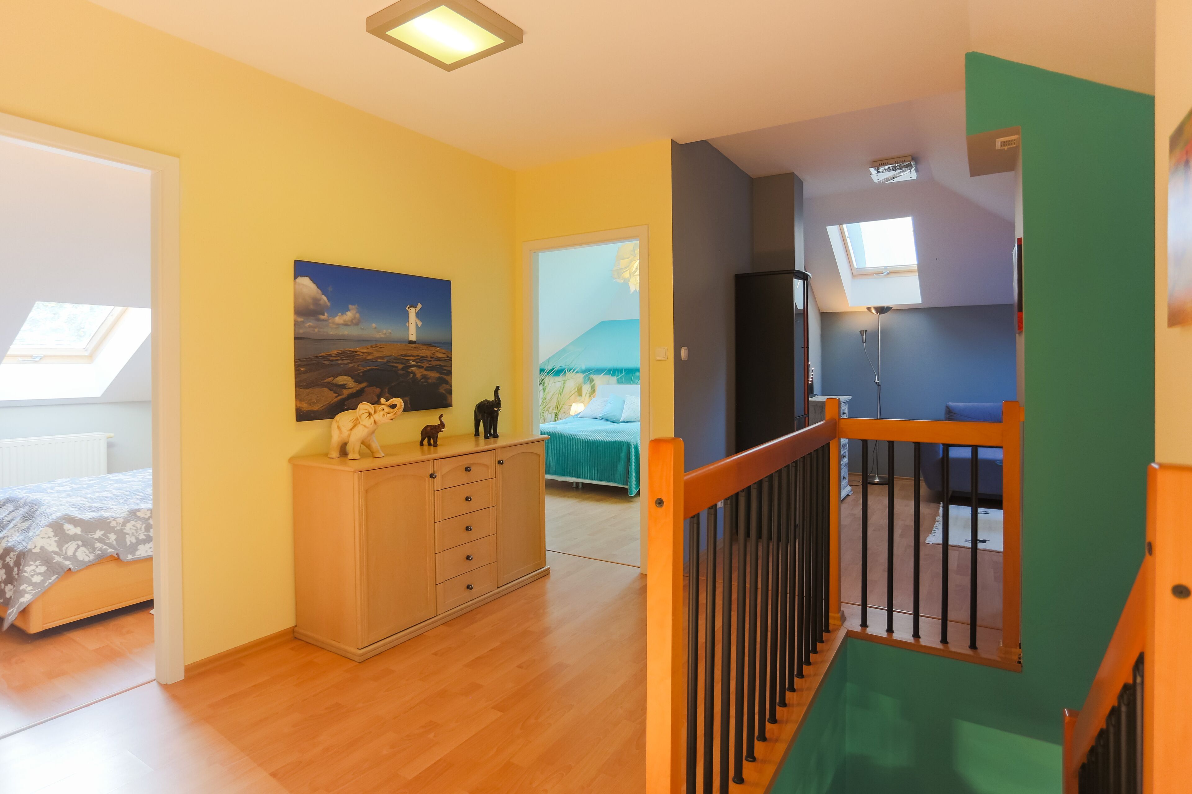A room with a bed, a dresser, a painting, and a staircase.