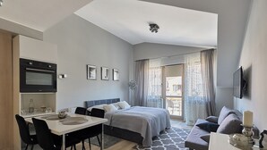 A modern bedroom with a bed, a desk, and a kitchenette.