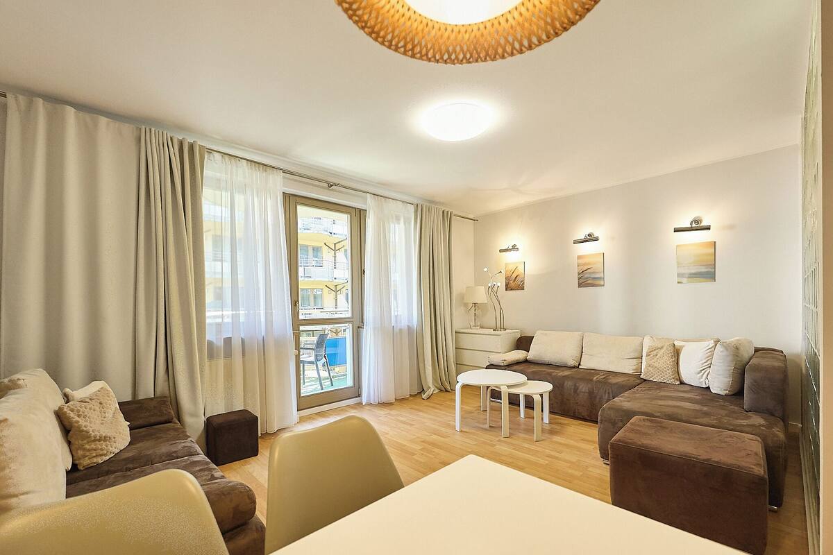 Ein Wohnzimmer mit einer Sofagarnitur, einem Esstisch und Blick durch ein Fenster.