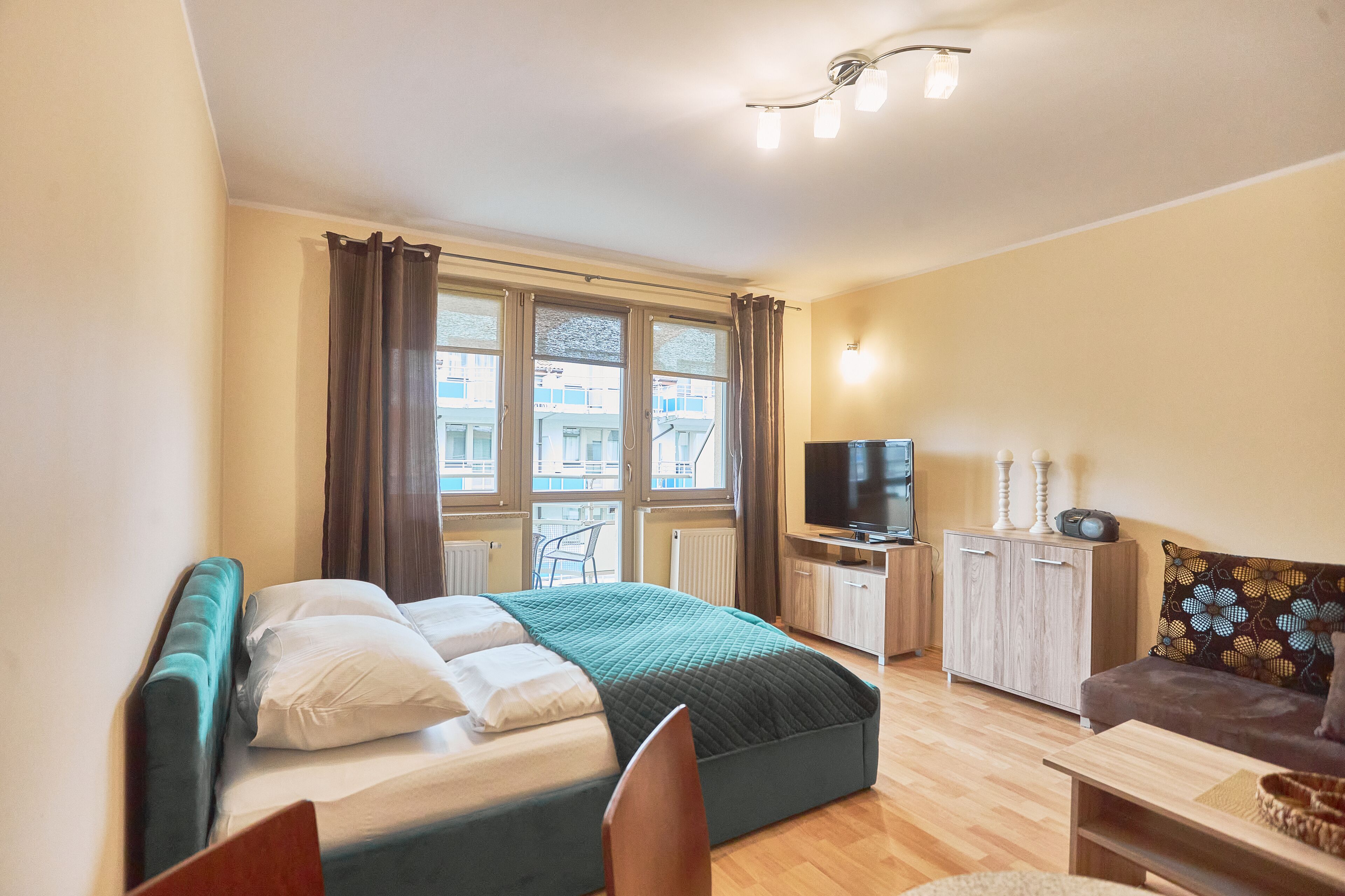 A bedroom with a bed, a TV, a sofa, and a window with curtains.