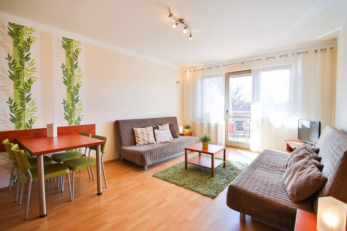 Ein Wohnzimmer mit einer Couch, einem Esstisch mit Stühlen, einem Couchtisch und einem Fernseher.