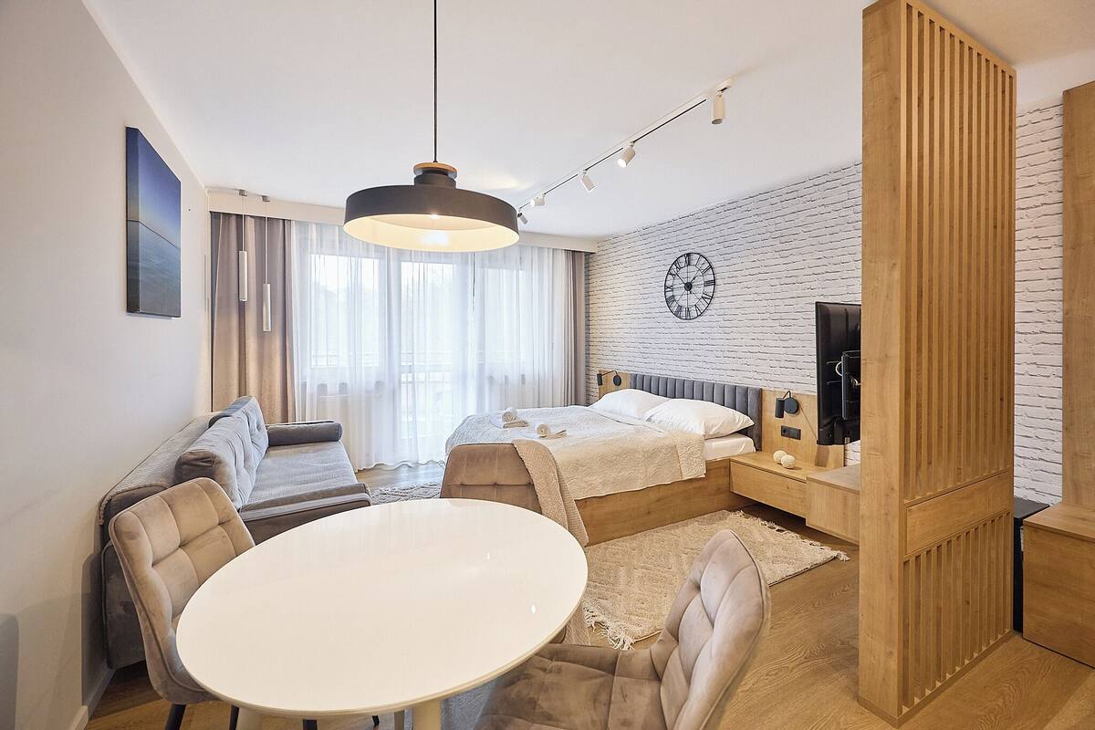 Ein modernes Hotelzimmer mit Bett, Sofa, Esstisch und einem großen Fenster mit Vorhängen.