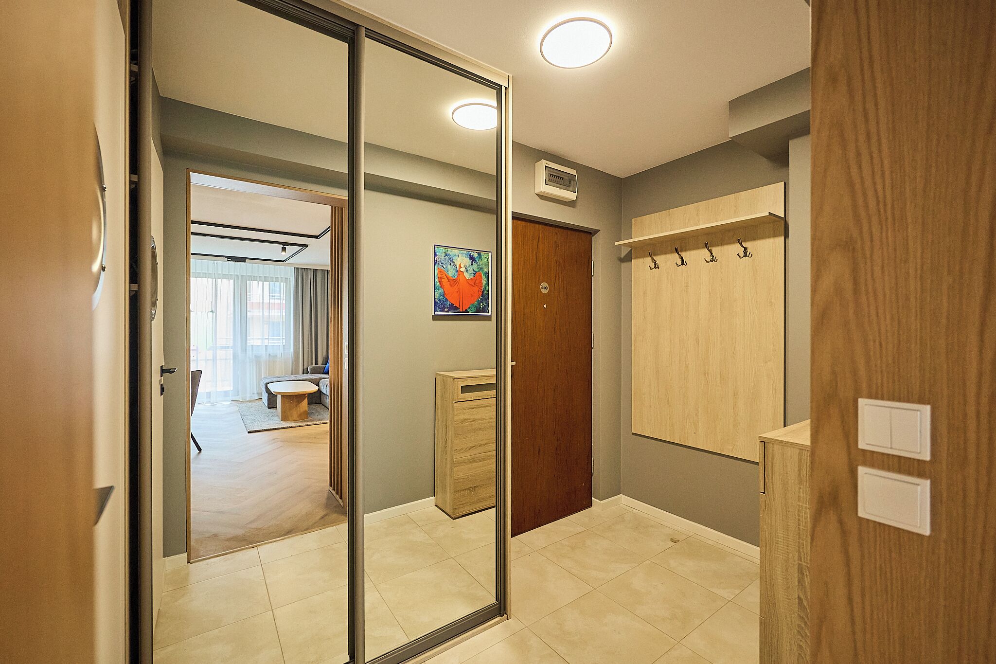 En modern inredning med en skjutdörr i glas som leder till ett vardagsrum, en garderob i trä och en väggmonterad klädhängare.