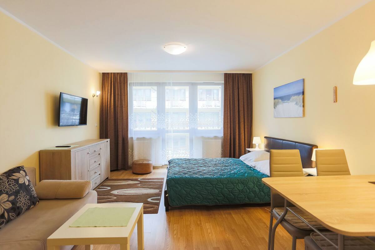 Ein Hotelzimmer mit Bett, Sofa, Tisch, Fernseher und einem Fenster mit Vorhängen.