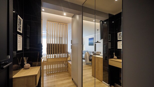 A modern hotel lobby with a wooden reception desk, a glass partition, and a view of the interior.